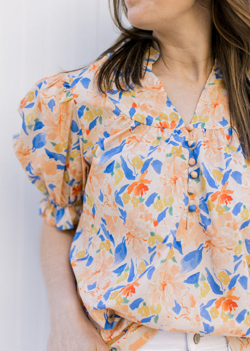 Close up of v-neck with buttons and bubble short sleeves on a peach floral top.