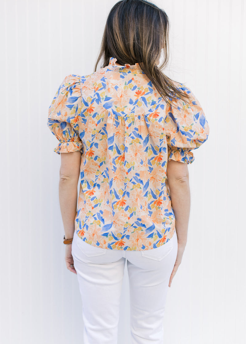 Back view of Model wearing a peach top with a floral pattern, v-neck and bubble short sleeves.