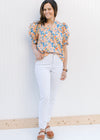 Model wearing white jeans and a peach top with a floral pattern, v-neck and bubble short sleeves.