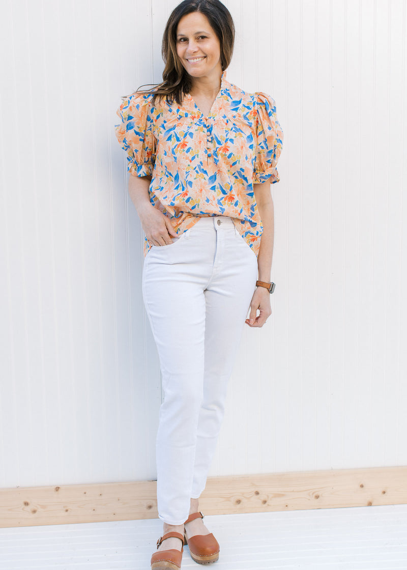 Model wearing white jeans and a peach top with a floral pattern, v-neck and bubble short sleeves.
