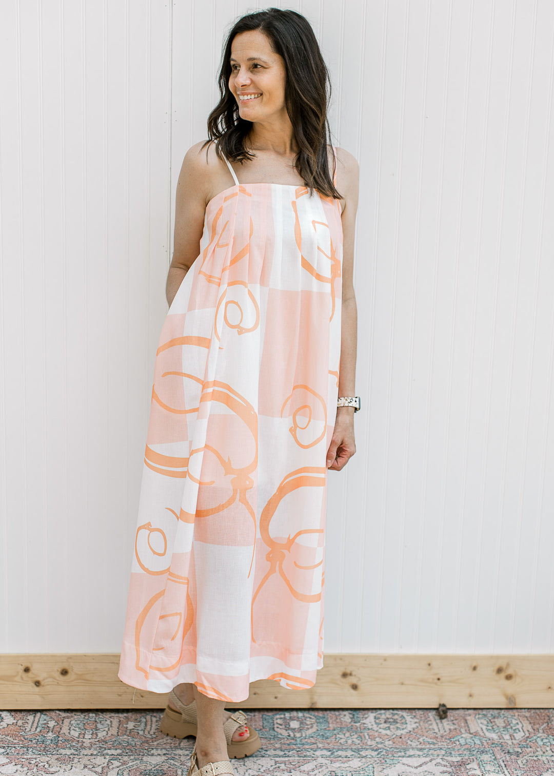 Model wearing a white maxi with peach abstract pattern and adjustable spaghetti straps.