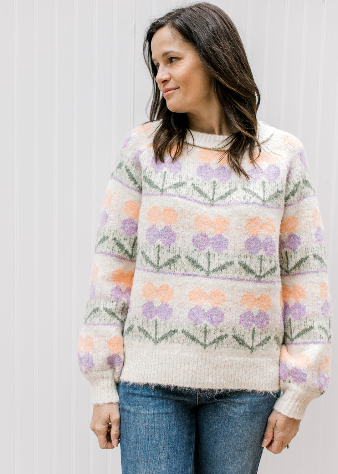 Model wearing a cream sweater with purple and peach flowers, a round neck and long sleeves. 