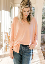 Model wearing a peach long sleeve top with side slits and ribbed detail at the neck, cuff and hem. 