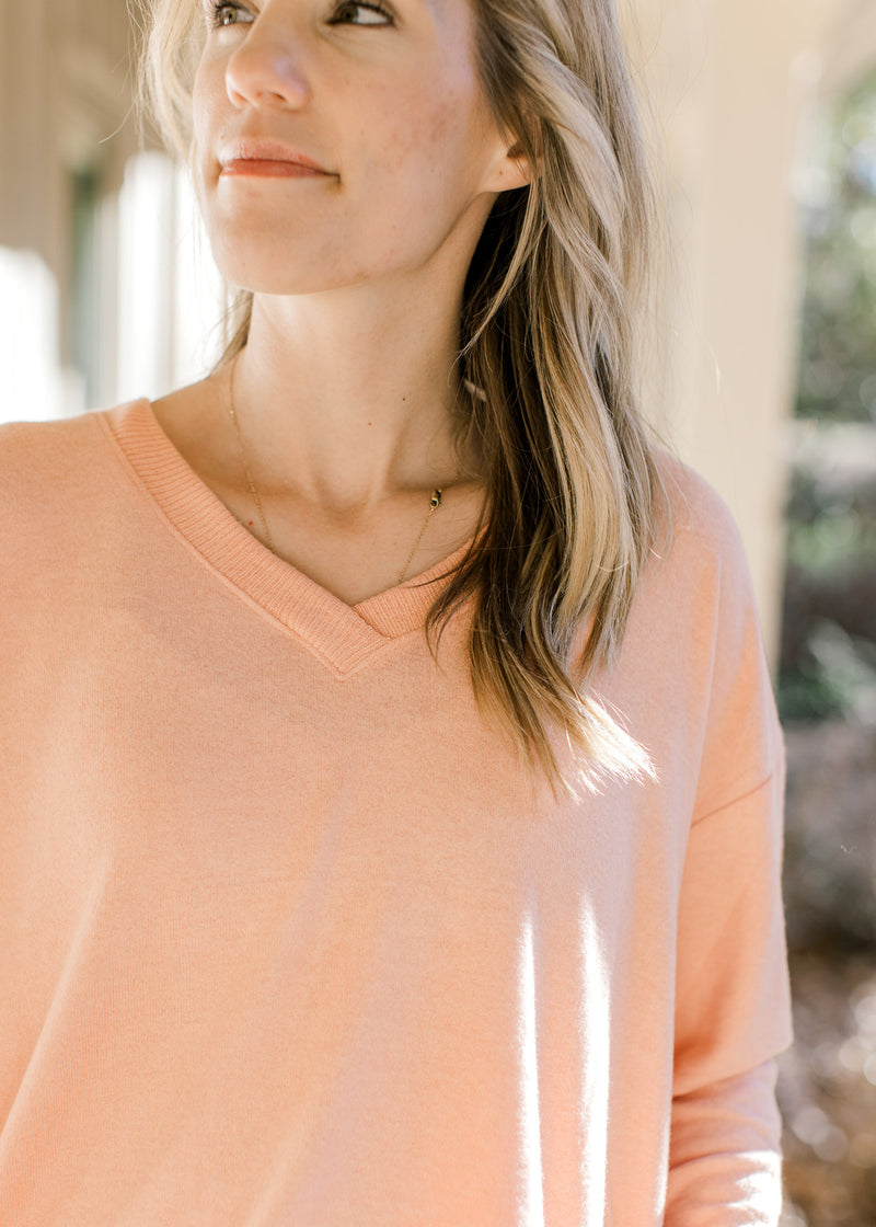 Close up of ribbed detail on round neck of a peach long sleeve top with side slits. 