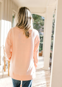 Back view of Model wearing a peach long sleeve top with side slits and ribbed detail.