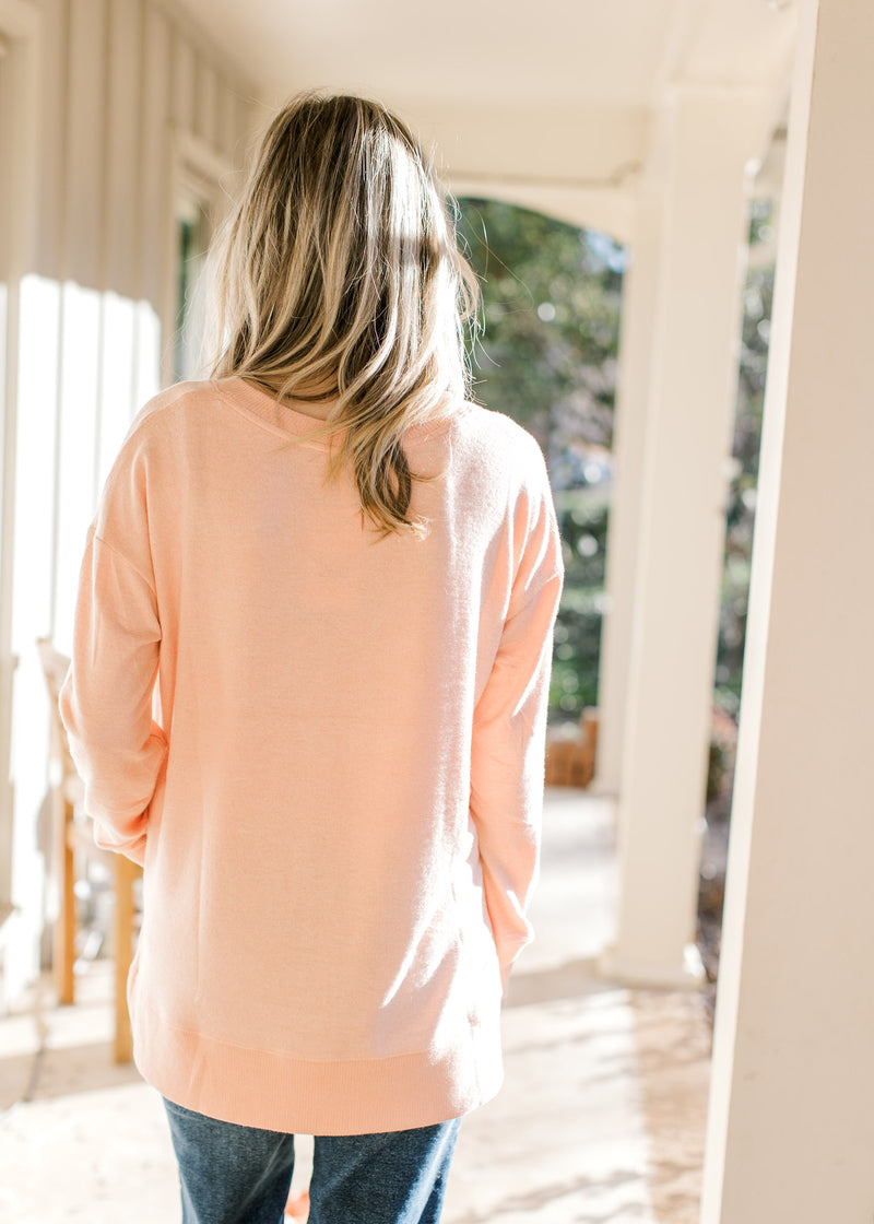 Back view of Model wearing a peach long sleeve top with side slits and ribbed detail.