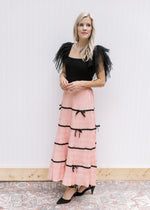 Model wearing a black top, heels and a peach skirt with plisse bow and pleated fabric.