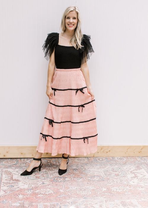Model wearing a peach skirt with plisse bows, elastic waist and pleated fabric. 