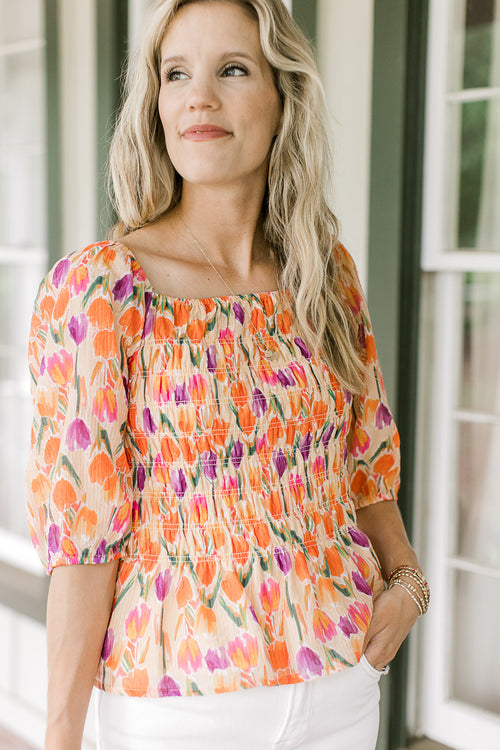 Model wearing a peach top with purple, gold and green tulips, a smocked bodice and a square neck.