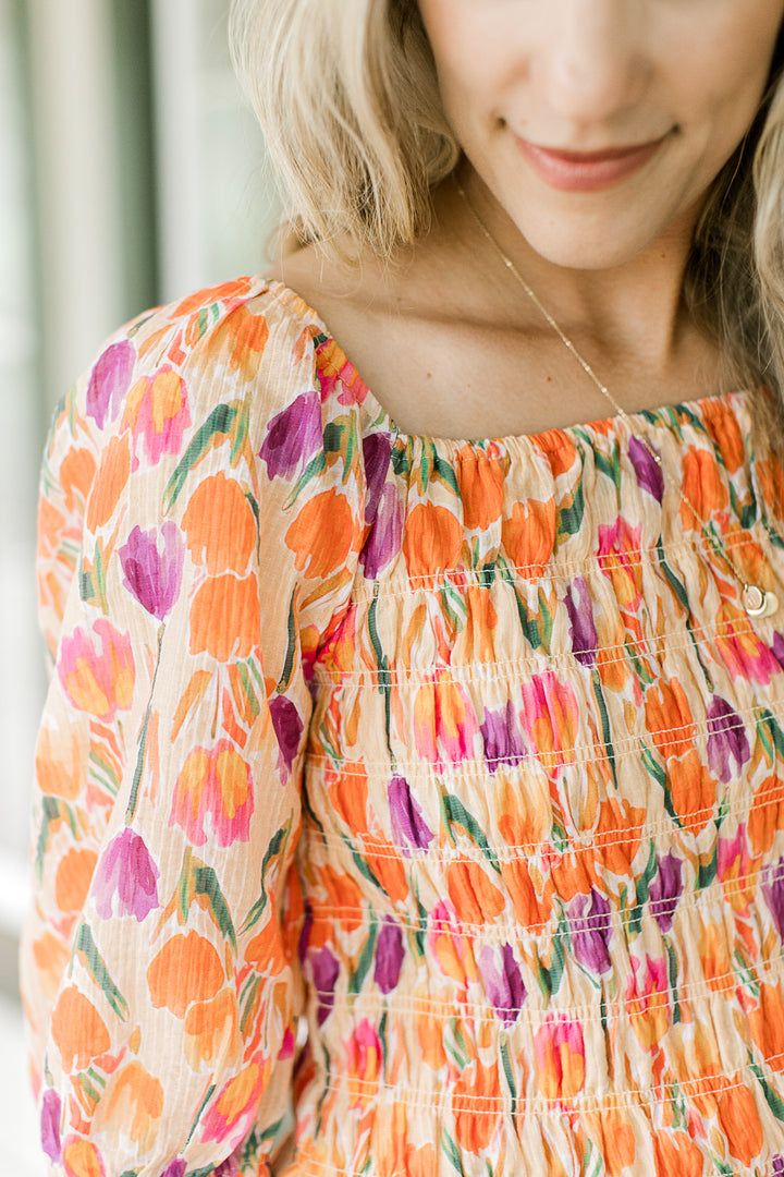 Close up of smocked bodice and square neck on a peach top with purple, gold and green tulips.