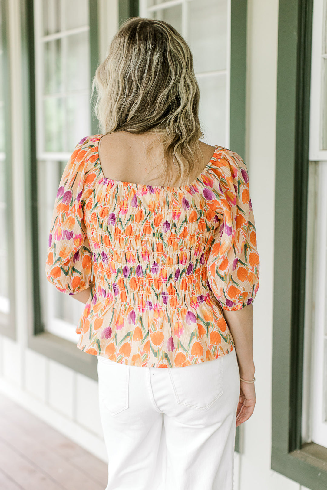 Back view of Model wearing a peach top with purple, gold and green tulips and a square neck.