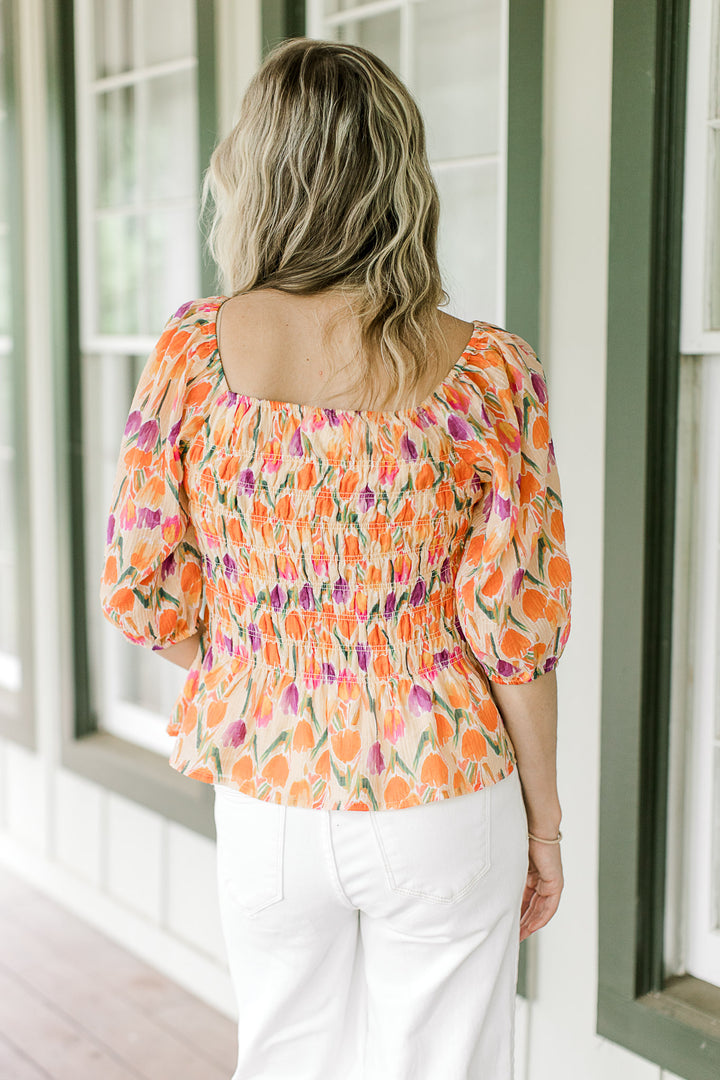 Back view of Model wearing a peach top with purple, gold and green tulips and a square neck.