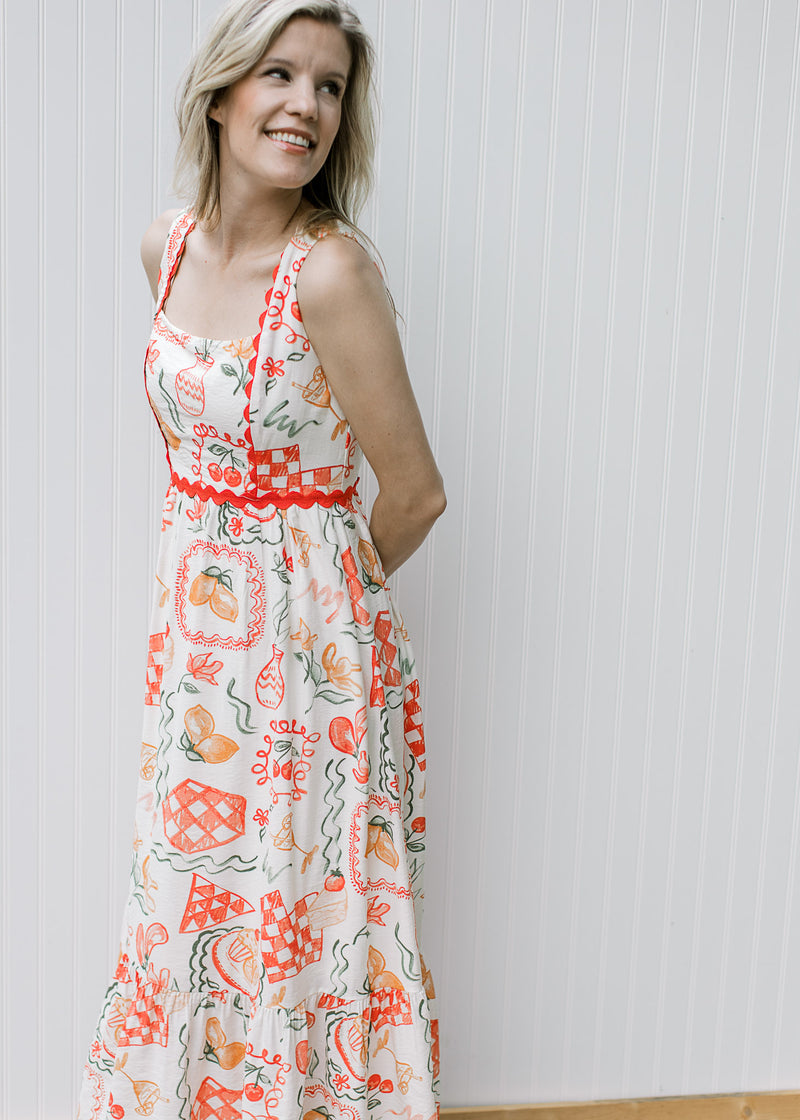 Model wearing a cream, square neck maxi with bright coral fruit, pots and treats and ric-rac trim. 