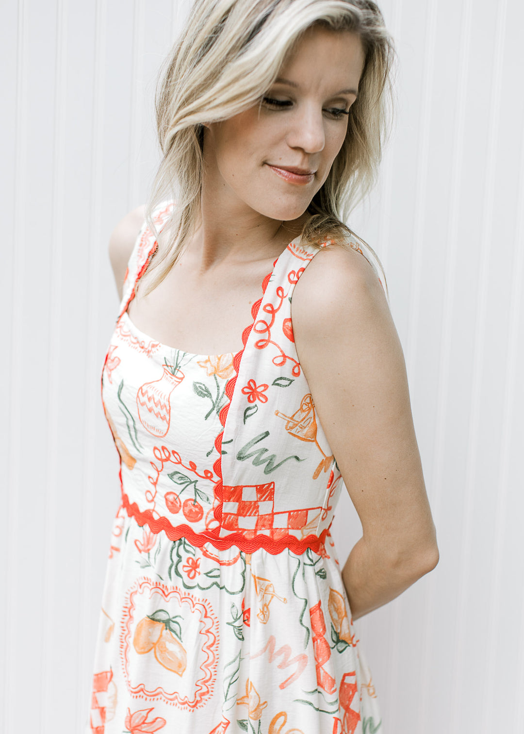 Close up of square neck and bright coral ric-rac on a cream dress with fruit, pots and treats.