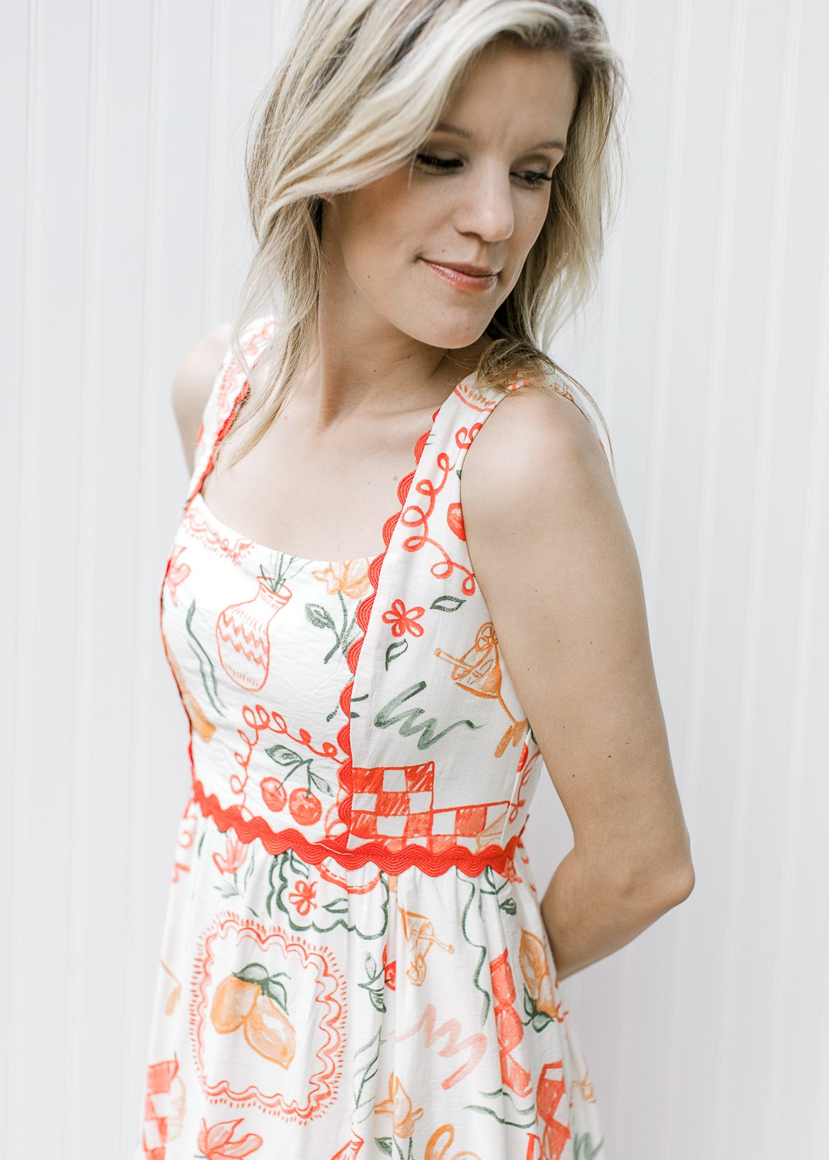 Close up of square neck and bright coral ric-rac on a cream dress with fruit, pots and treats.