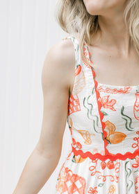 Close up of  bright coral ric-rac on a sleeveless cream dress with fruit, pots and treats.
