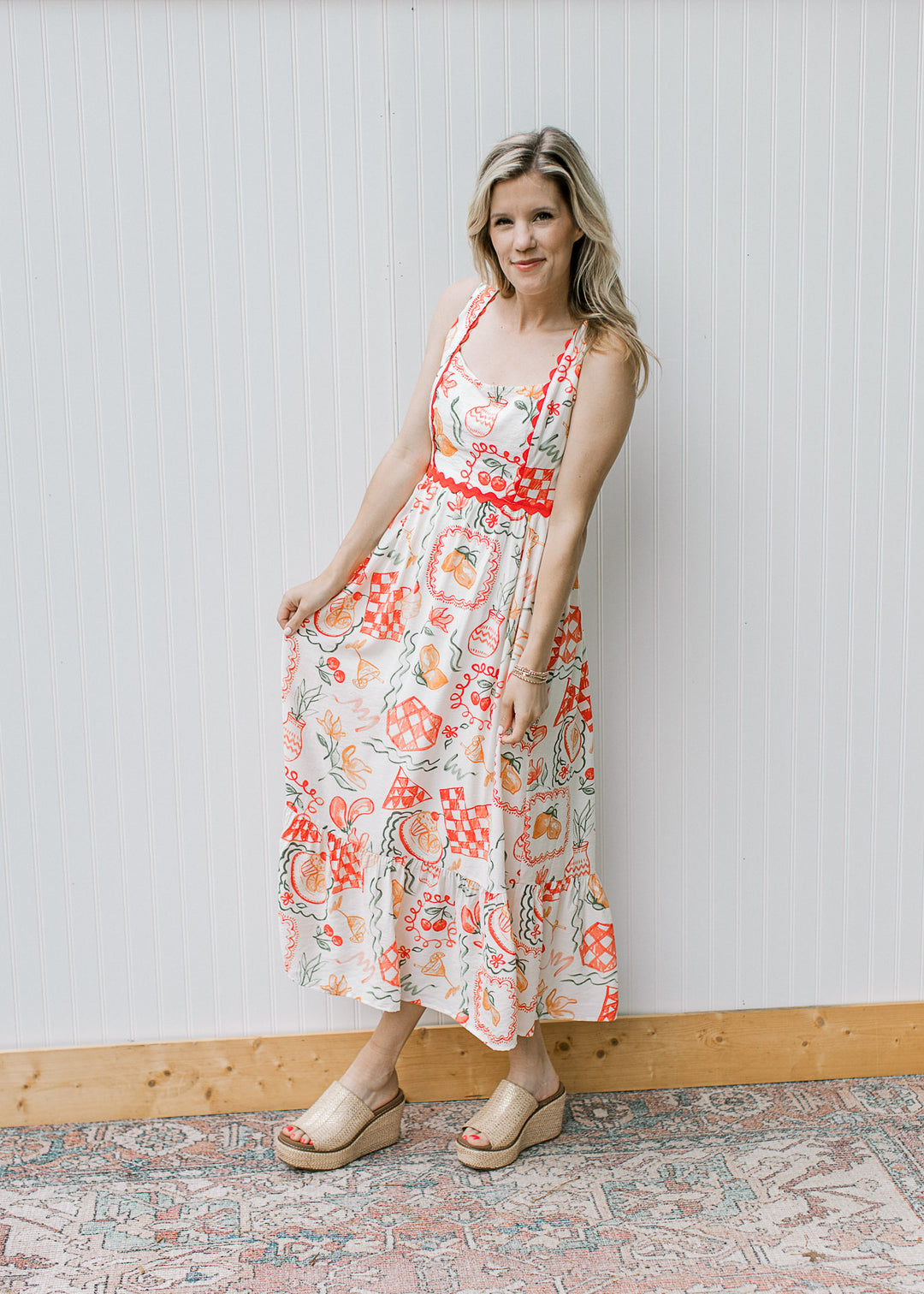 Model wearing wedges and a cream, square neck maxi with fruit, pots and treats and ric-rac trim. 