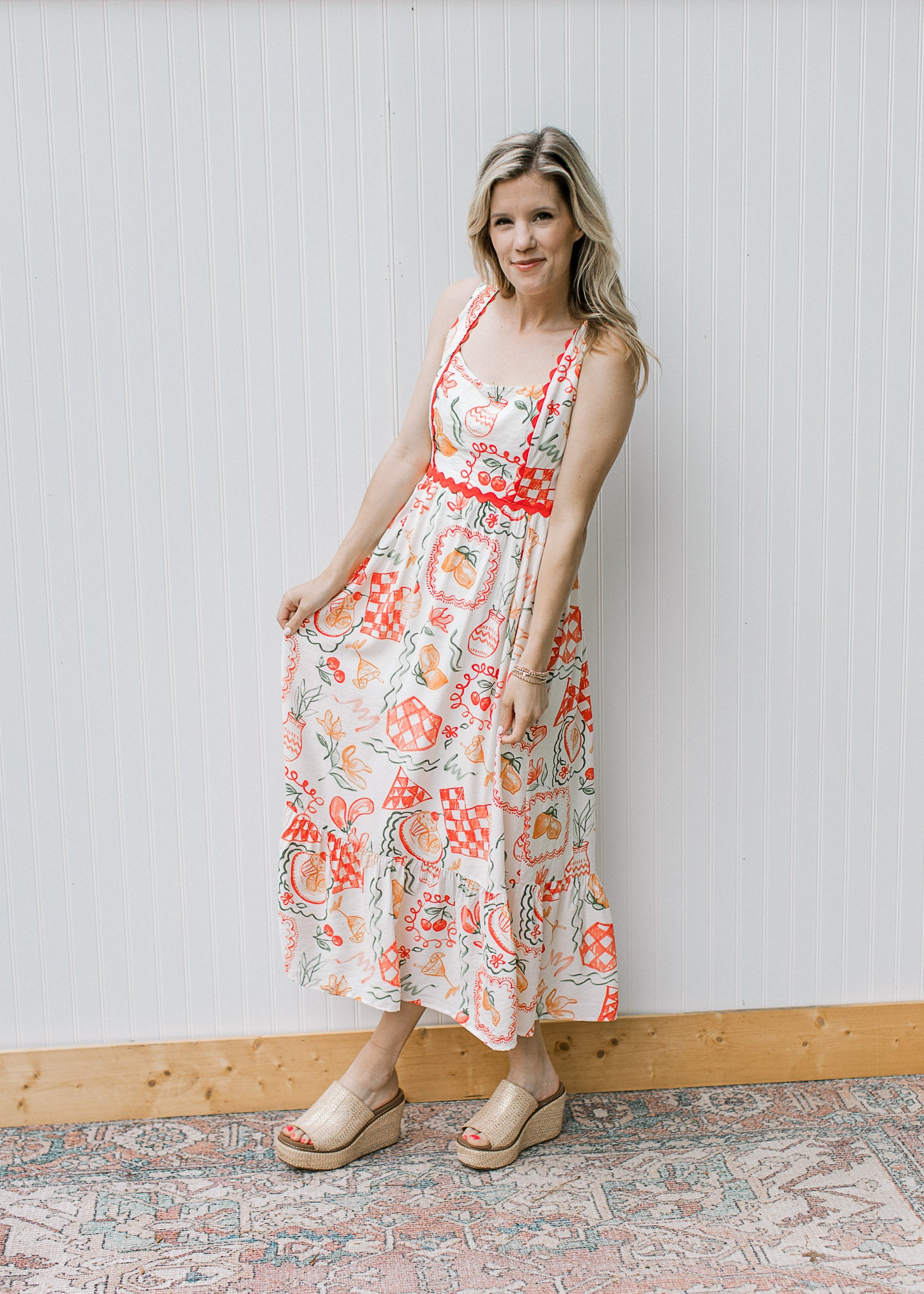 Model wearing wedges and a cream, square neck maxi with fruit, pots and treats and ric-rac trim. 