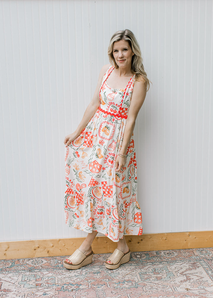Model wearing wedges and a cream, square neck maxi with fruit, pots and treats and ric-rac trim. 