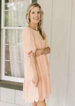 Model wearing a peach dress with scalloped hem and short sleeves and tiers. 