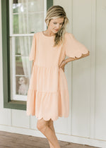 Model wearing a peach tiered dress with scalloped hem and short sleeves. 