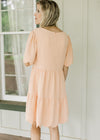 Back view of a model wearing a peach dress with scalloped short sleeves and hem and a zipper.