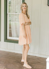 Model wearing flats with a peach tiered dress with scalloped short sleeves and hem.