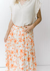 Model wearing a cream midi pleated skirt with a white and peach floral pattern and an elastic waist.