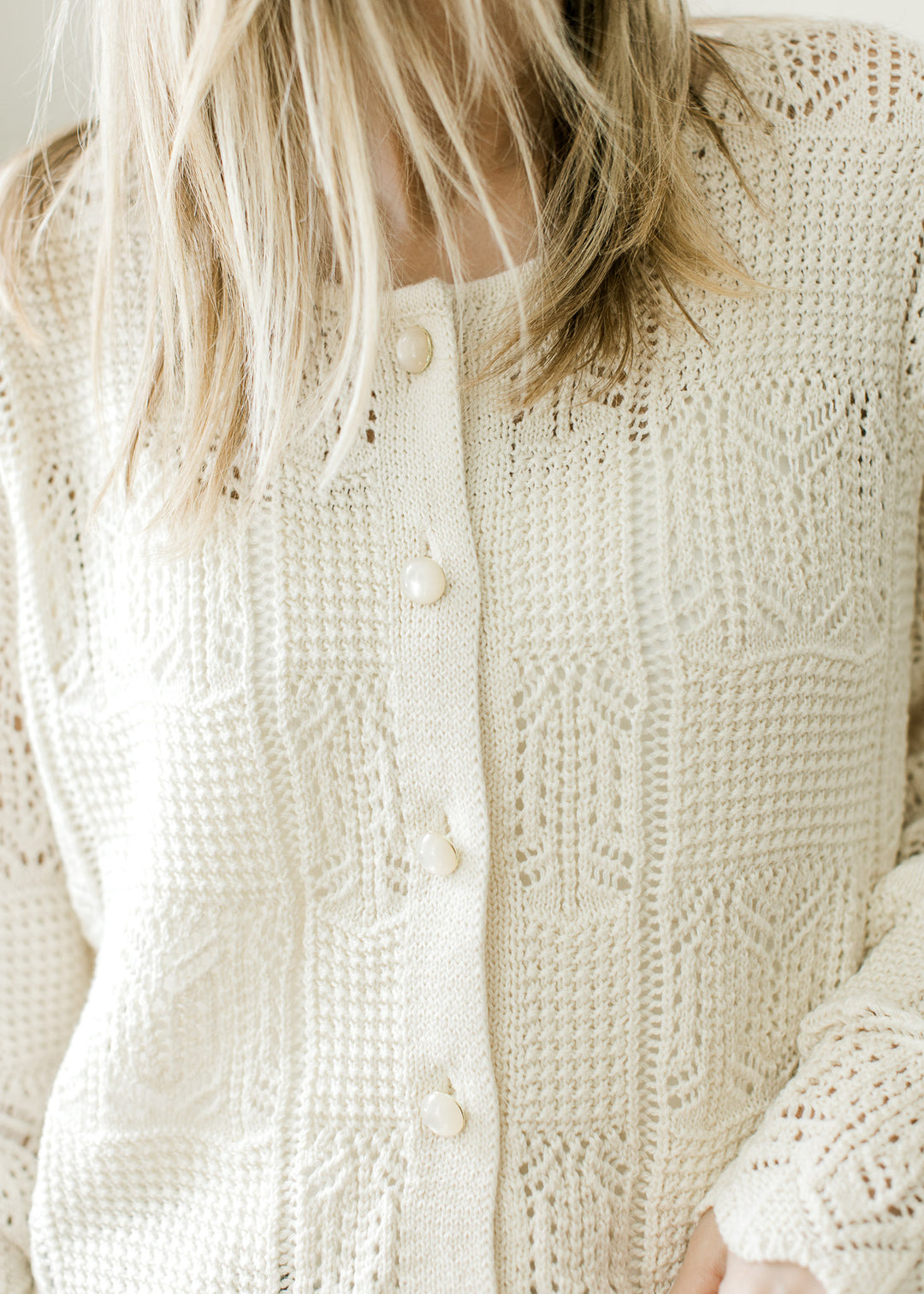 Close up of square knit pattern and pearl button front on a cream long sleeve cardigan. 