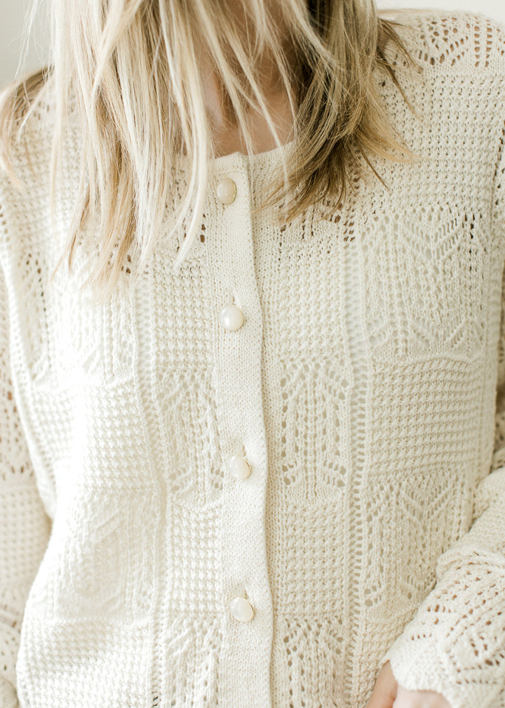 Close up of square knit pattern and pearl button front on a cream long sleeve cardigan. 