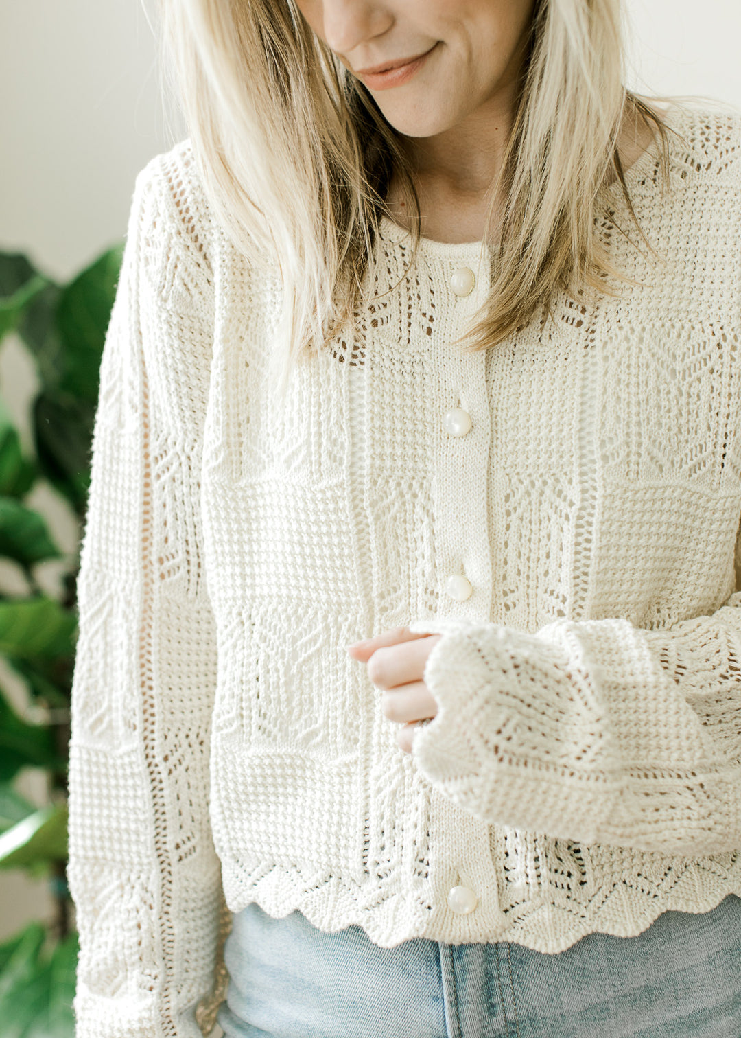 Model wearing a long sleeve cream knit with pearl button front and scalloped hem and cuff. 