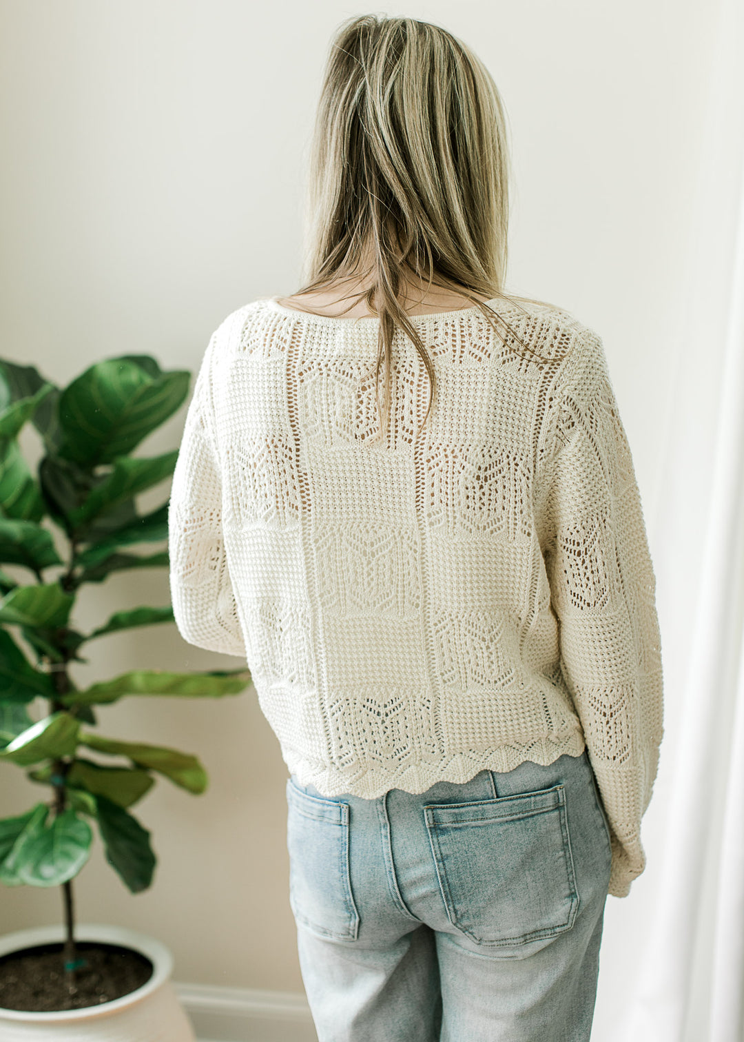 Back view of Model wearing a long sleeve cream cardigan with square knit pattern and scalloped hem.