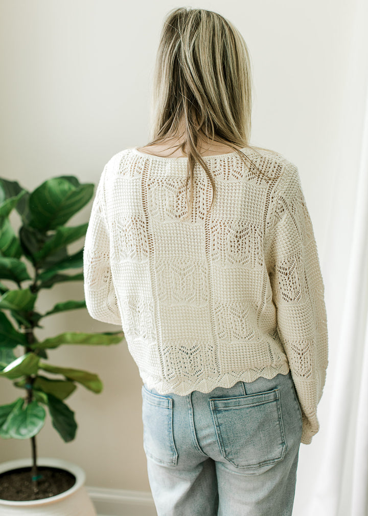 Back view of Model wearing a long sleeve cream cardigan with square knit pattern and scalloped hem.
