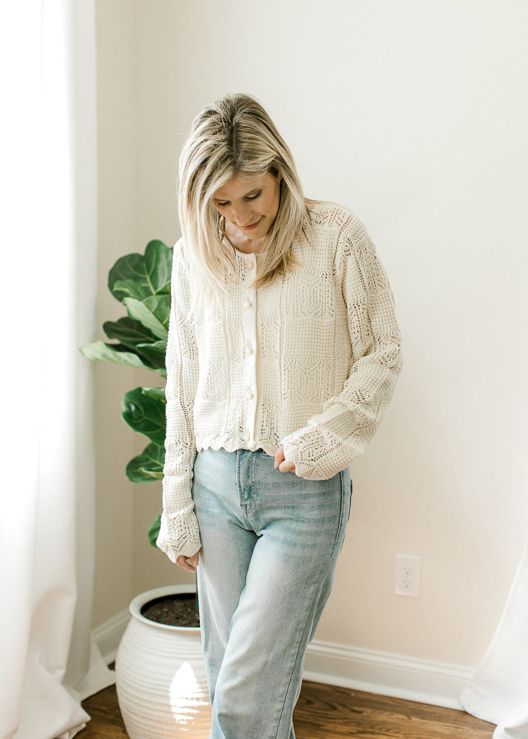 Model wearing jeans and a long sleeve cream cardigan with round neck and pearl button front. 