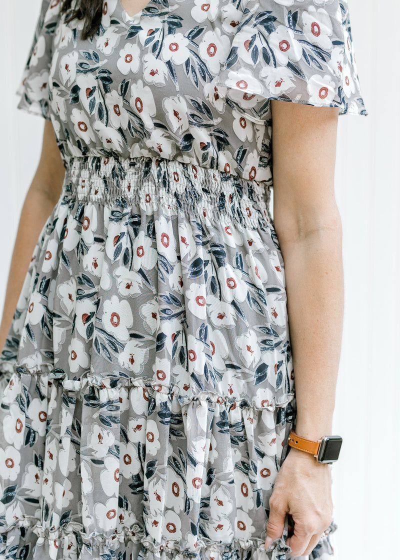 Close up view of elastic waistband on a model wearing a gray dress with a cream floral pattern. 