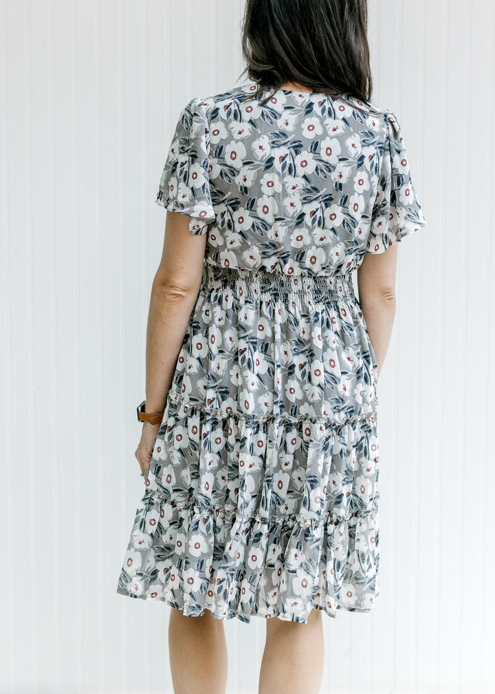 Back view of model wearing a gray dress with a cream floral pattern and a tiered skirt. 
