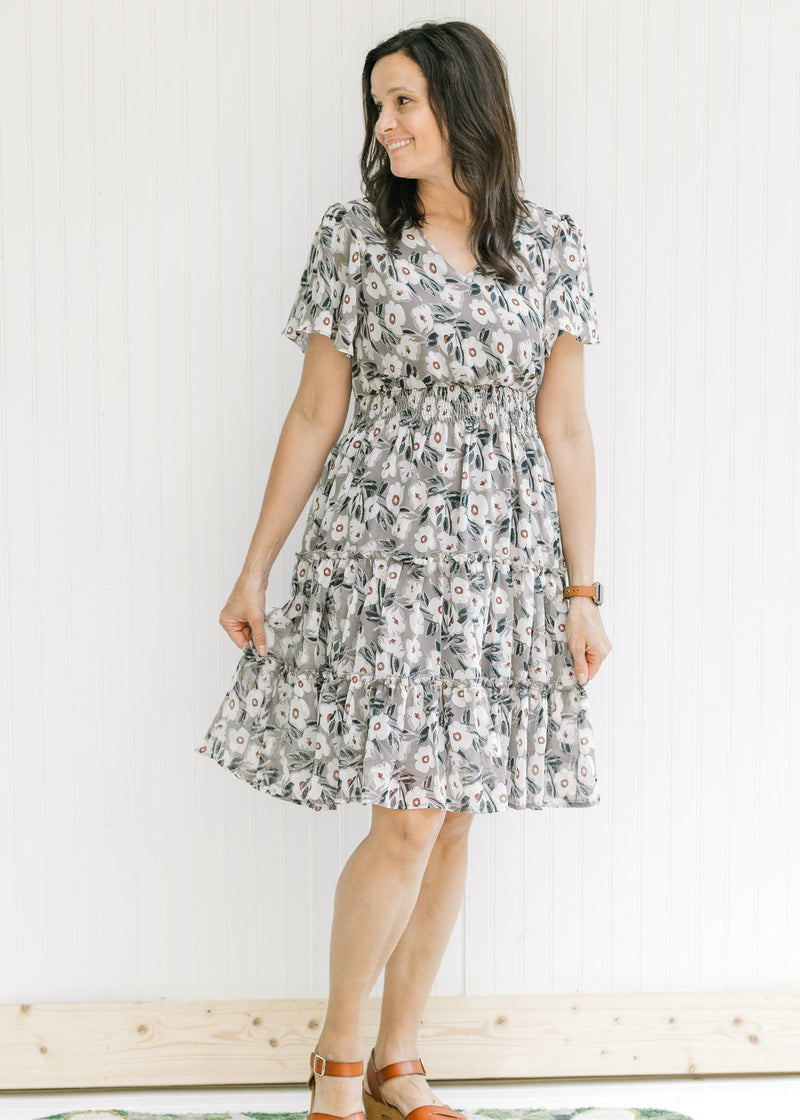 Model wearing a gray above the knee dress with a cream floral pattern and flutter short sleeves. 