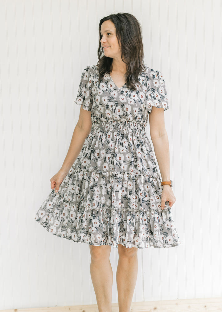 Model wearing a gray dress with a cream floral pattern, elastic waistband and flutter short sleeves.