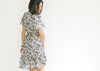 Back view of Model wearing a gray dress with a cream floral pattern and flutter short sleeves.