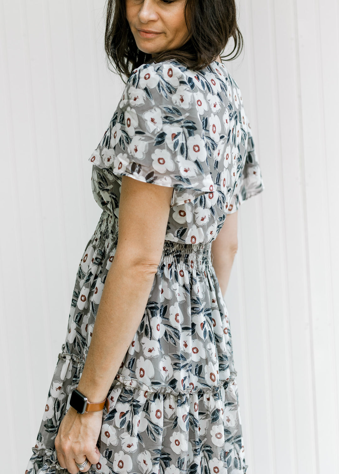 Back of a gray dress with a cream floral pattern, flutter short sleeves and a tiered skirt. 