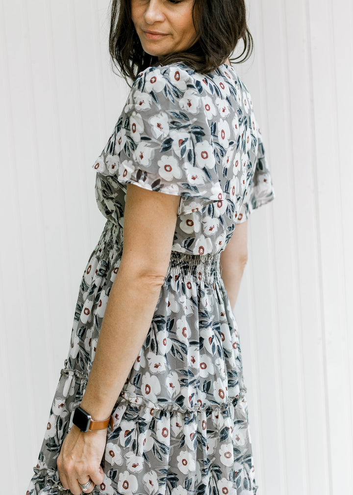 Back of a gray dress with a cream floral pattern, flutter short sleeves and a tiered skirt. 