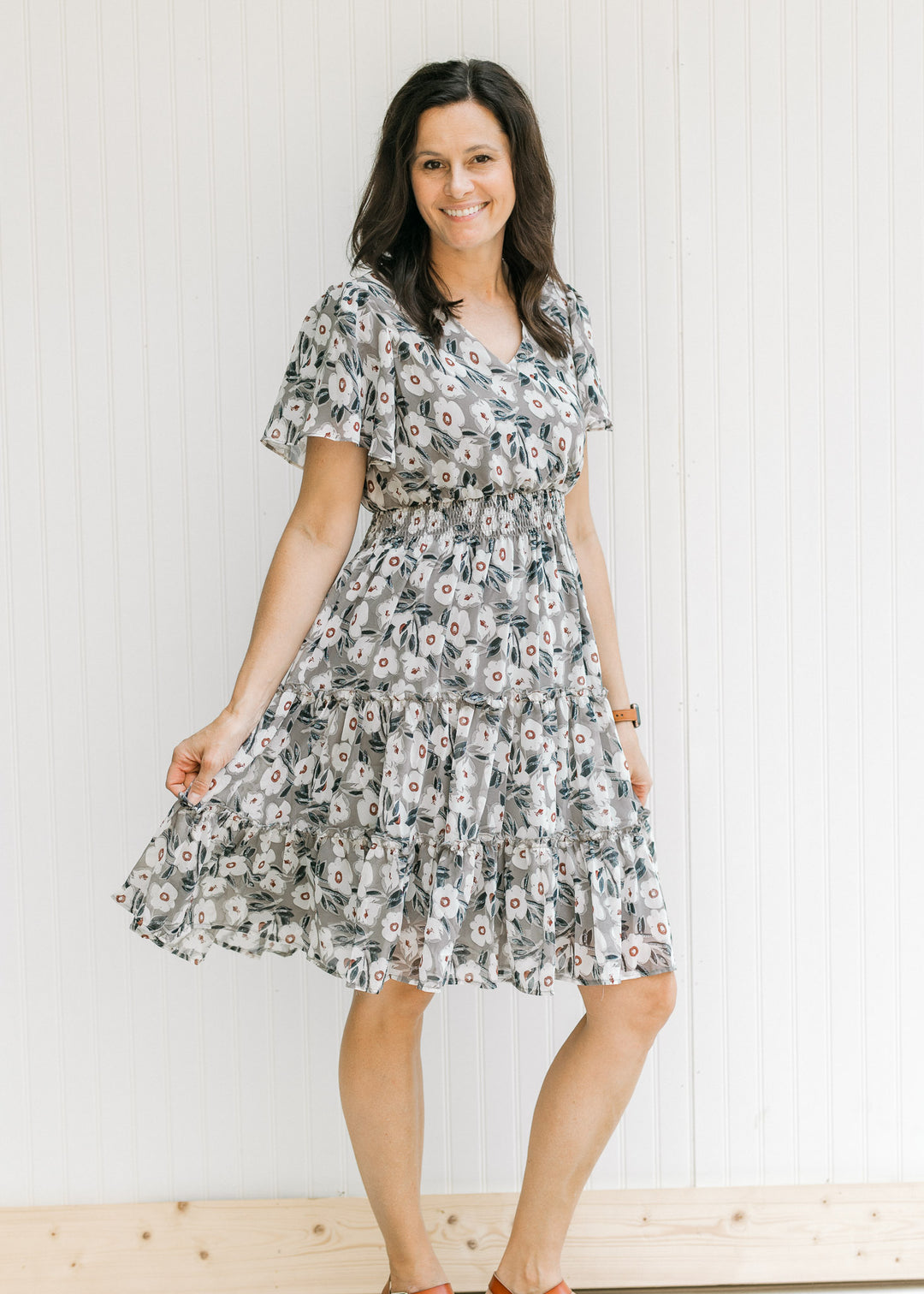 Model wearing a gray dress with a cream floral pattern, tiered skirt and an elastic waistband. 