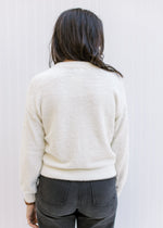 Back view of Model wearing an ivory sweater with pearl embellishments, round neck and long sleeves. 
