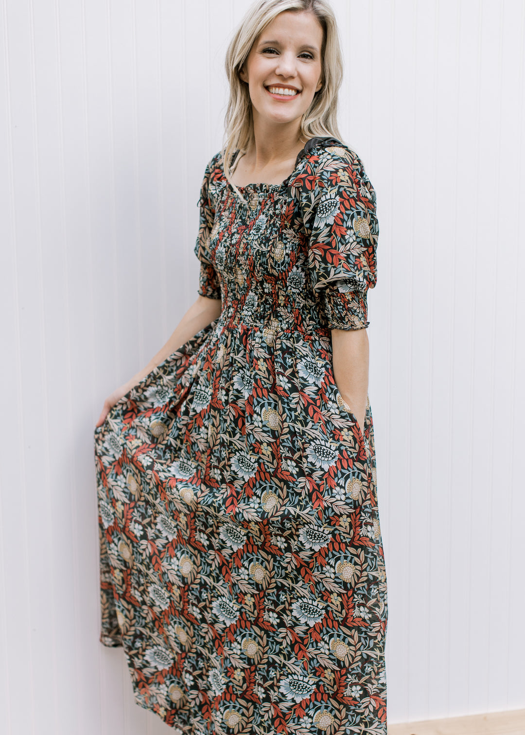 Model wearing a deep rust colored dress with a floral pattern, smocked bodice and short sleeves. 