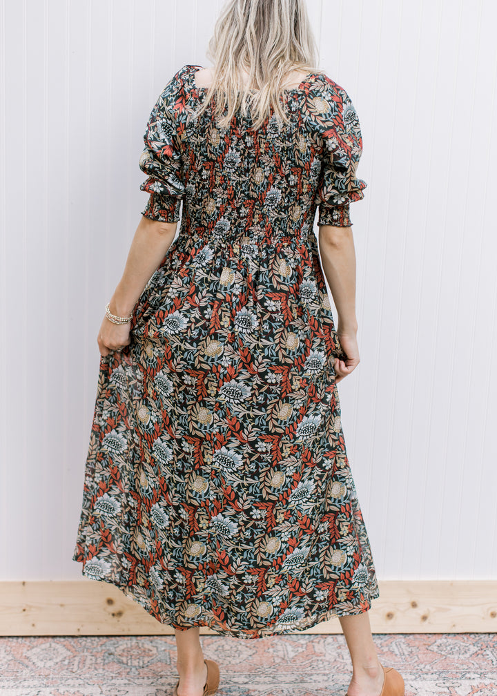Back view of Model wearing a deep rust short sleeve dress with a floral pattern and smocked bodice.