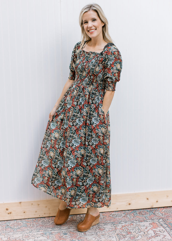 Model wearing mules with a deep rust dress with a floral pattern, smocked bodice and short sleeves. 