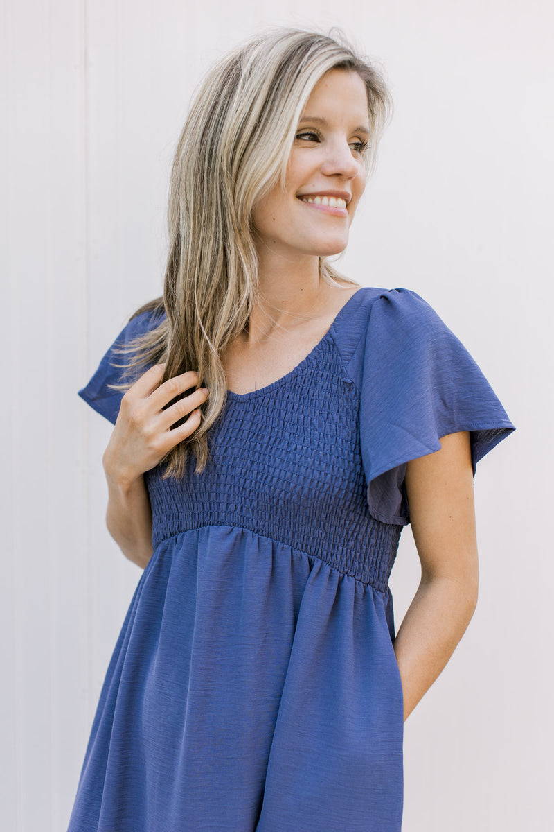 Close up of smocked bodice and flutter short sleeves on a cobalt blue midi dress with a v-neck.
