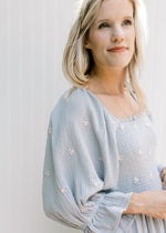 Close up of square neck and 3/4 poet sleeves on a blue dress with pink embroidered flowers.