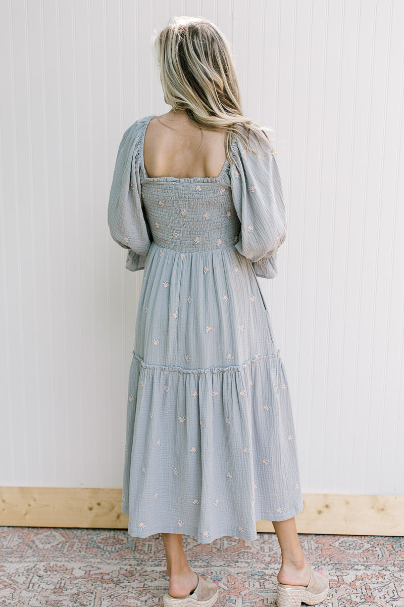 Back view of Model wearing a blue dress with pink flowers, smocked bodice and square neck.