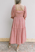 Back view of Model wearing a rose dress with pink flowers, poet sleeves and a smocked bodice.